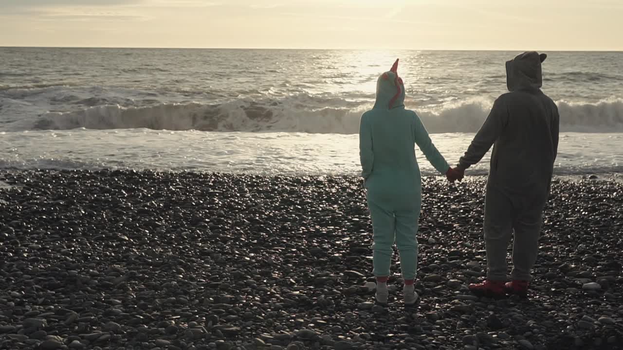 해가 지는 동안 자갈 해변 에 있는 동물 의 파자마 를 입은 부부