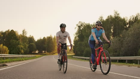 A-man-and-a-woman-on-bicycles-ride-down-the-road-at-sunset-together-in-slow-motion.-The-couple-travels-by-Bicycle.-Sports-Cycling-helmets.