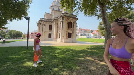 women playing tennis in a park with a historical building in the background