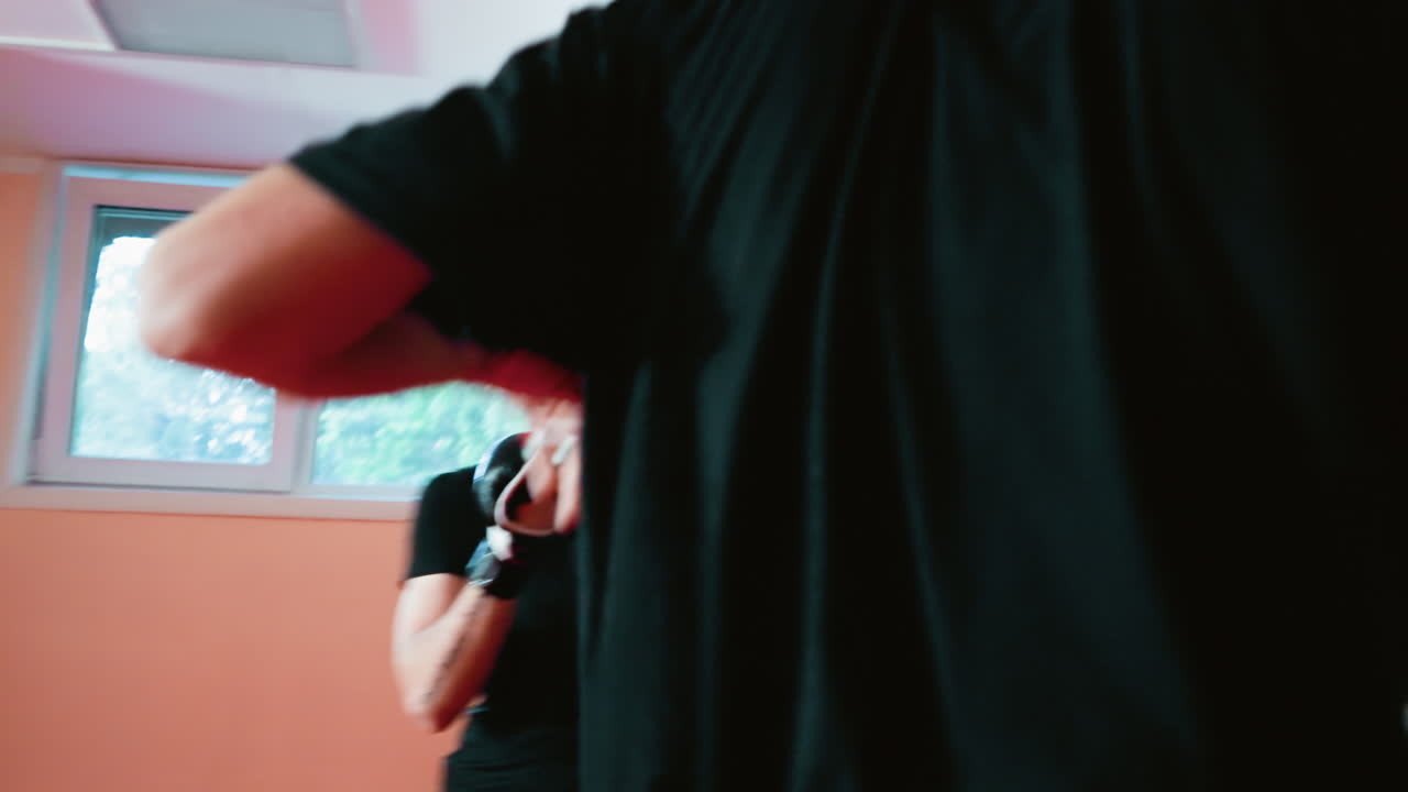 Karate practitioners facing each other inside gym, focused on sparring session, dressed in black training attire with gloves, martial arts technique during practice fight
