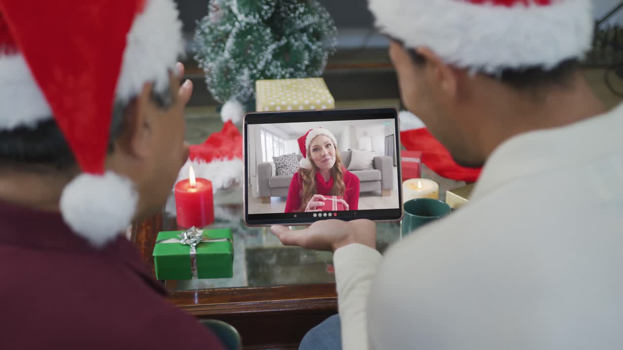 padre y hijo biraciales con sombreros de santa usando una tableta para una videollamada de navidad con una mujer en la pantalla