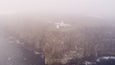 Aerial-reverse-shot-of-a-stunning-clifftop-lighthouse-in-Scotland-on-a-misty-morning