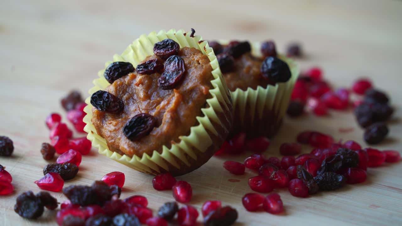 Panorâmica ascendente revelando muffins de abóbora com cranberries e passas. Muffins de abóbora veganos recém-assados, saindo do forno, feitos com abóbora assada de verdade em uma tigela, uma receita saudável e sem laticínios.