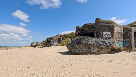 wide shot of historic graffiti-covered concrete bunker on sandy beach under blue sky, daylight