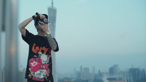 slow motion shot of a young asian photographer capturing urban downtown from the rooftop in the early morning