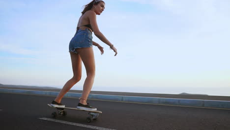 amid the picturesque sunset, a woman rides her skateboard on a road, captured in slow motion. mountains and a beautiful sky complete the backdrop, and she's in shorts