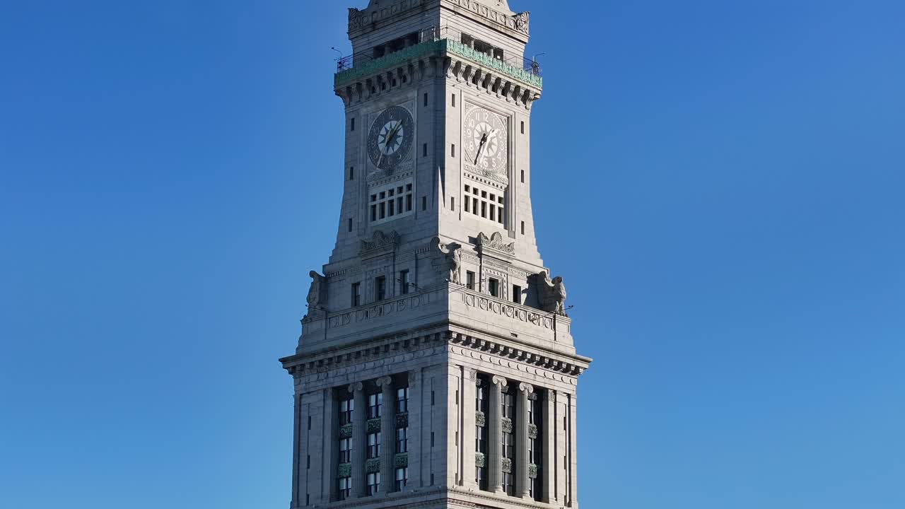 Custom House Tower clock stands tall in downtown Boston. Ornate stone corners guard the apex. Aerial zoom, tilt up.
