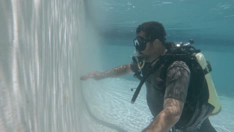 a professional pool cleaner in scuba equipment cleans a pool while underwater