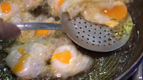 closeup of a man frying small quail eggs in a pan with plenty of oil