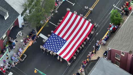 Eine-Kleine-Menschenmenge-Sieht-Zu,-Wie-Im-Rahmen-Der-Parade-Am-4.-Juli-Eine-Große-Flagge-Vorbeigetragen-Wird