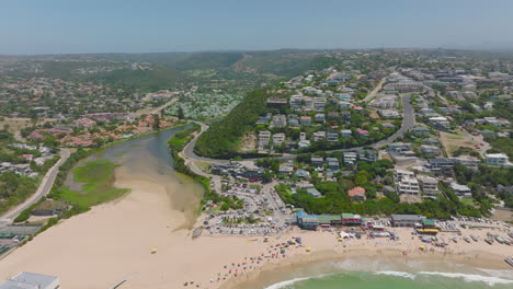 River-flowing-through-coastal-town-and-its-estuary-to-sea-at-sand-beach.-Summer-vacation-destination-on-sunny-day.-Plettenberg-Bay,-South-Africa