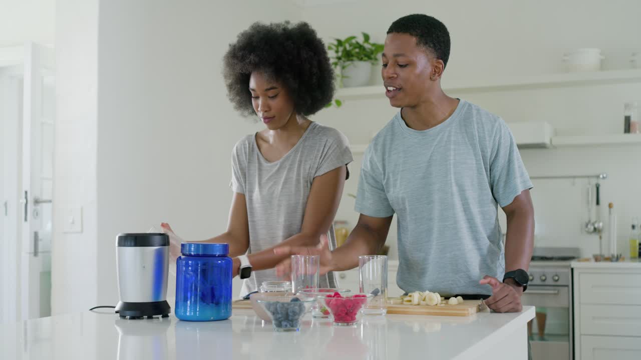 African American couple facing, scooping from blue container and preparing smoothies at island