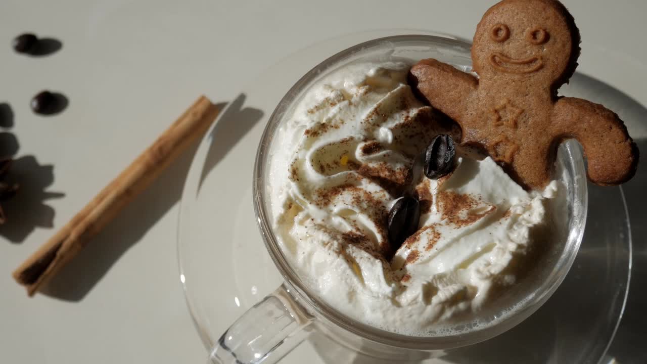 Top-down close-up of pumpkin spice latte with whipped cream, cinnamon powder and gingerbread man cookie under natural light