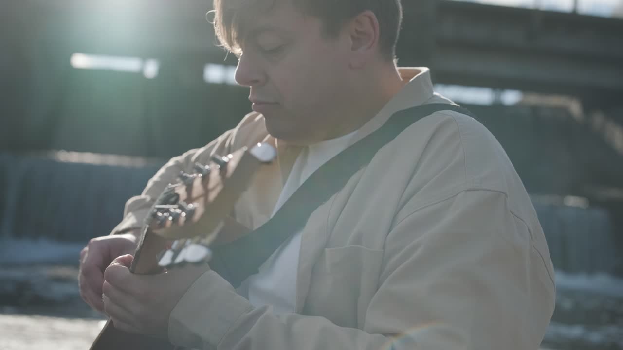 바위의 배경에 산의 강변에 앉아 기타를 연주하는 젊은이. 자유의 개념, 휴식 장소.