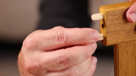 Hands insert dowels into wooden furniture joints under soft lighting, demonstrating precise craftsmanship and assembly techniques
