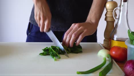 person slicing fresh arugula using a sharp knife in a cutting board - close up