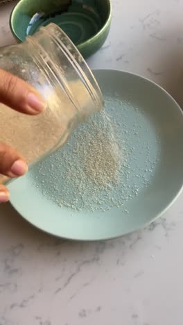 Vertical-video-of-cane-sugar-being-poured-onto-a-plate-to-roll-vegan-donuts-in-it