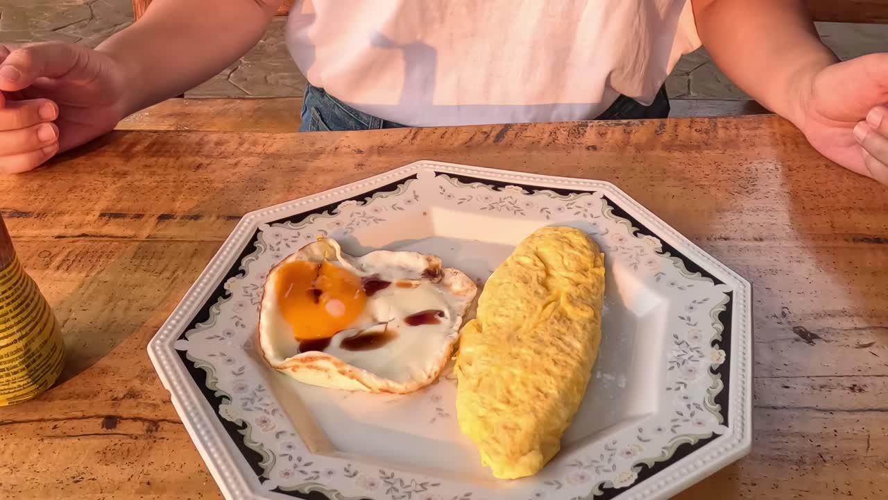 Close-up of hands seasoning an omelette and sunny-side-up egg on a decorative plate.