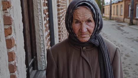 weathered face reflecting life experience, senior woman standing confidently in rural village street, wearing traditional headscarf and coat with profound dignity