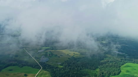 Green-landscape-of-forest-and-fields,-aerial-view-above-fluffy-clouds