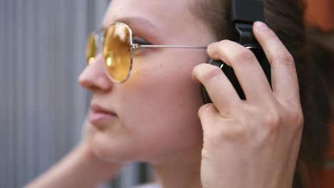 young caucasian woman with black headphones outdoors on sunny summer day. girl listening to music wearing yellow sunglasses