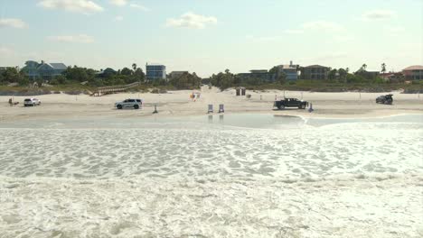 Ein-Niedriger-Blick-Nach-Vorne-Auf-New-Smyrna-Beach,-Florida,-Mit-Autos,-Die-Auf-Dem-Sand-Fahren