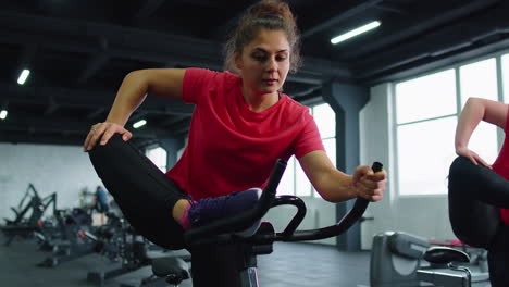 Grupo-De-Amigas-Sonrientes-Clase-De-Mujeres-Haciendo-Ejercicio,-Entrenando,-Estirándose-En-Bicicleta-Estática-En-El-Gimnasio