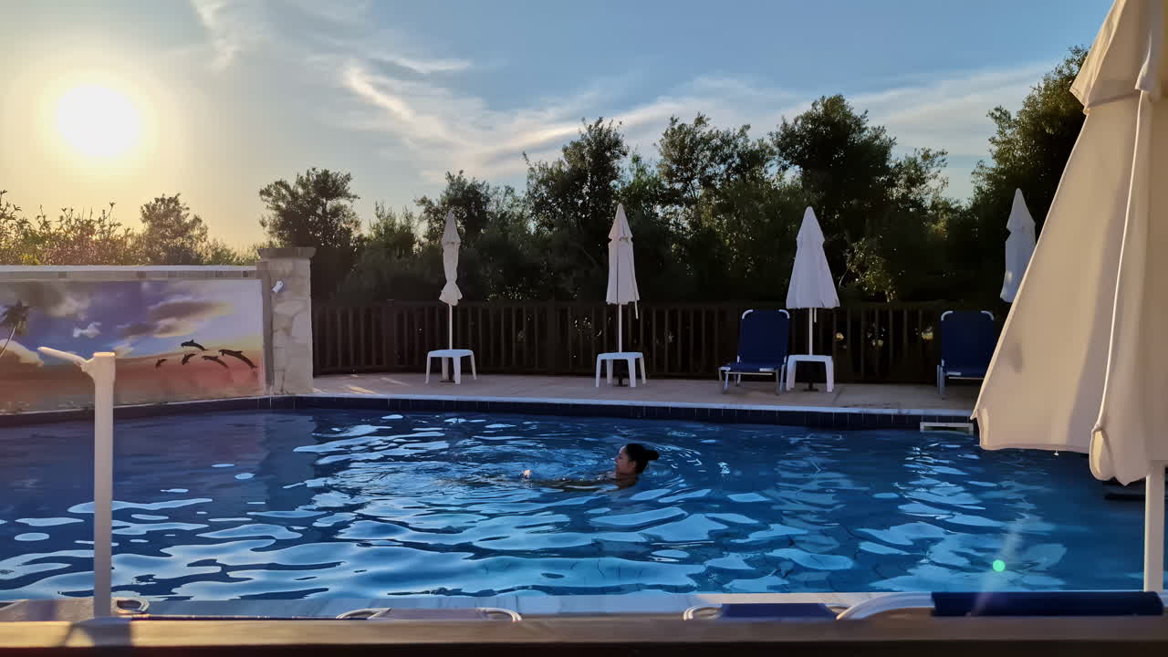 Slowmotion-optagelse af en kvinde, der svømmer i en pool på et luksusresort og spa med solen skinnende klart i baggrunden