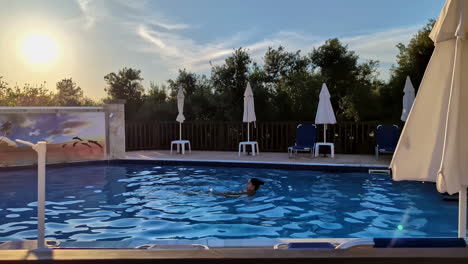 Slow-motion-shot-of-a-woman-swimming-in-a-pool-at-luxury-resort-spa-with-sun-shinning-brightly-in-the-background