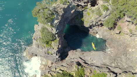 Kayakistas-Explorando-Un-Hermoso-Arco-De-Formación-Rocosa-En-La-Costa-De-Nueva-Zelanda,-Aéreo