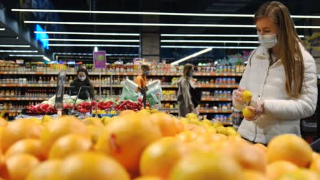 woman hand takes and examines fresh pink tomatoes on branch from display case at vegetable counter in supermarket.
