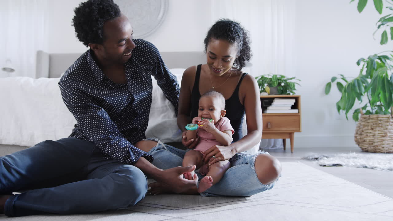 Loving Parents Playing With Baby Daughter Sitting On Floor In Bedroom