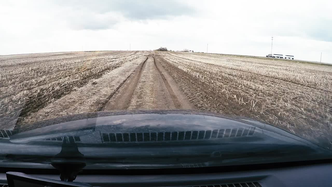 Dash cam view of an SUV rushing through a large puddle in a rural field getting water up and covering the windshield