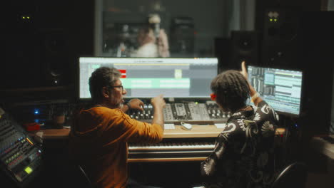 music producers mixing sound as singer recording vocals in audio studio