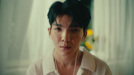 portrait of asiatic american mixed race young male while listening to music with earphone wearing white shirt