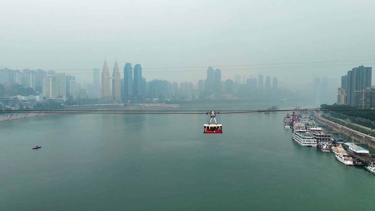 Aerial view following a cable car cabin above the river in Chongqing, China, showcasing the city’s skyline and the stunning landscape from a unique perspective during daytime.