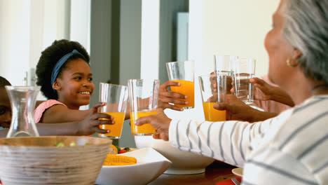 Side-view-of-black-multi-generation-family-toasting-glass-of-juice-and-water-at-dining-table-4k