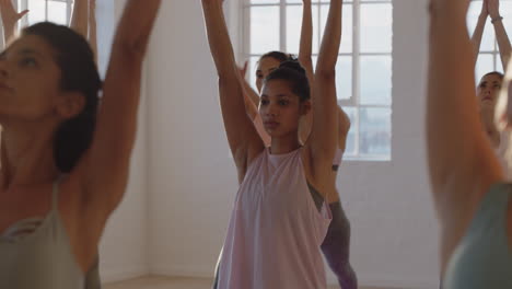 clase de yoga mujer de raza mixta saludable practicando pose guerrera con un grupo de mujeres hermosas disfrutando de un estilo de vida saludable haciendo ejercicio en el gimnasio al amanecer