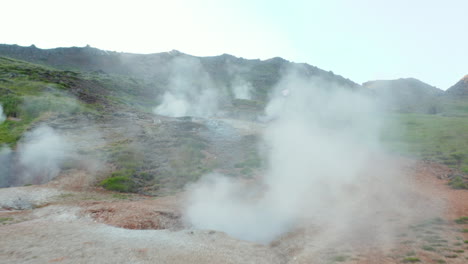 Drone-view-of-steaming-geothermal-hot-water-craters-in-Iceland.-Aerial-view-of-amazing-geothermal-landscape-with-tourist-exploring-wilderness