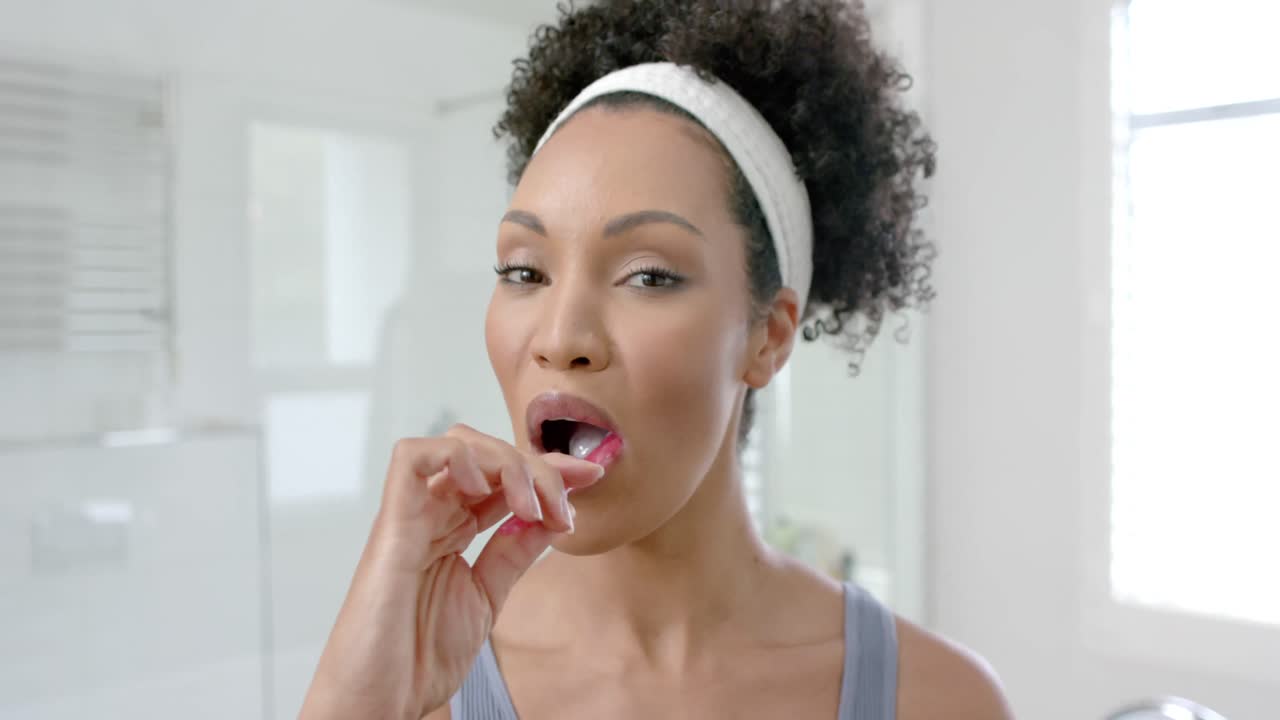 Happy biracial woman brushing teeth in bathroom, slow motion