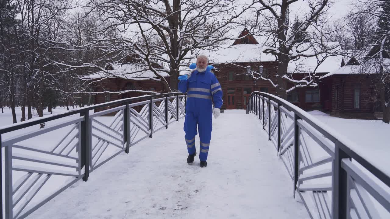 Old cleaner walking with shovel on shoulder.