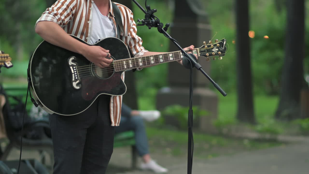 Mand, der spiller på en sort guitar i parken i dagslys