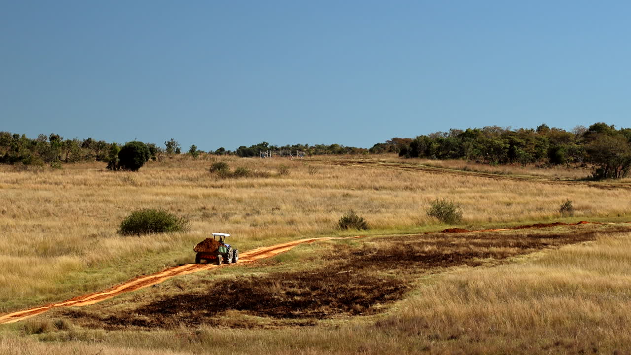 Tractor with trailer transport soil load on dirt road in remote bushveld, aerial