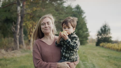 a happy mother carries a baby in her arms, he eats an apple. they walk through the farm, grapes grow nearby