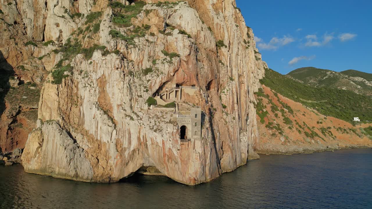 horizontal clip in 4k resolution of porto flavia in sardinia, drone is flying away from the port which remains visible throughout the shot. It's a sunny day with no overcast. Water is calm