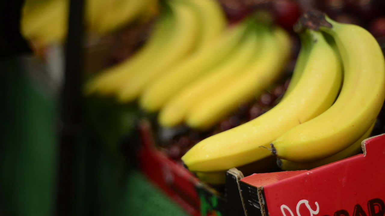 Cinematic close-up shot of ripe bananas being picked at a vibrant farmers market in England. Warm, natural lighting enhances the fresh, organic produce. Detailed view captures textures