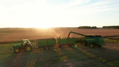 agriculture machines on field working, pouring crops into trunk, while person watches