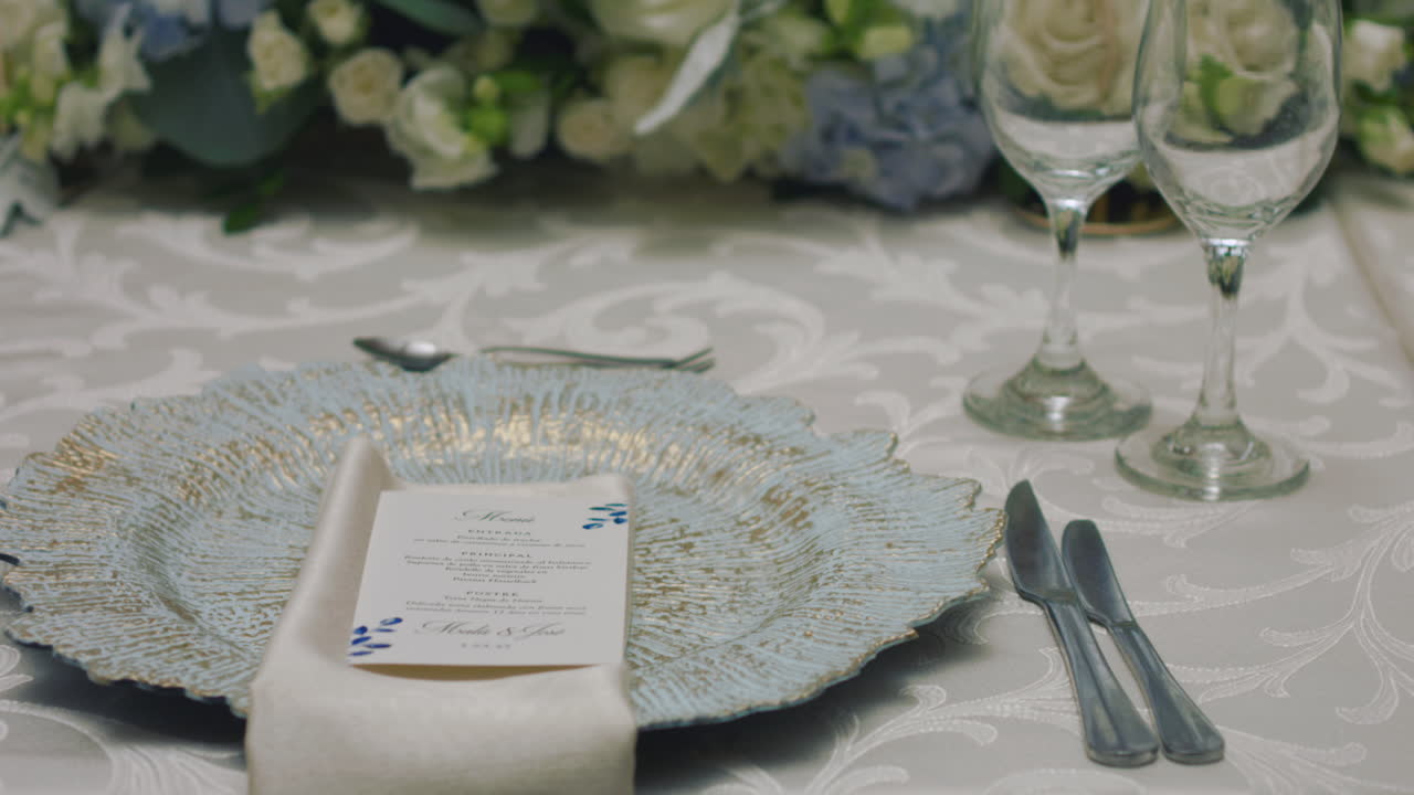 Close-up of a finely decorated wedding table with glass cups, a decorative plate, a white cloth napkin, and a menu on the plate.
