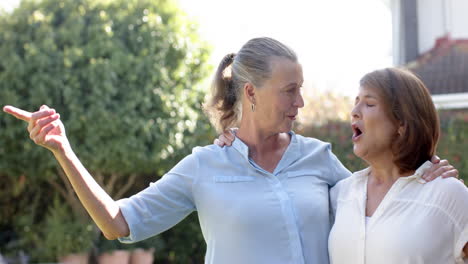 senior friends enjoying outdoor activity, pointing and waving in garden together