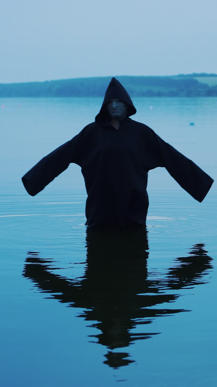 Terrible figure in a black robe in the water outdoor. Divination by Halloween Vertical video